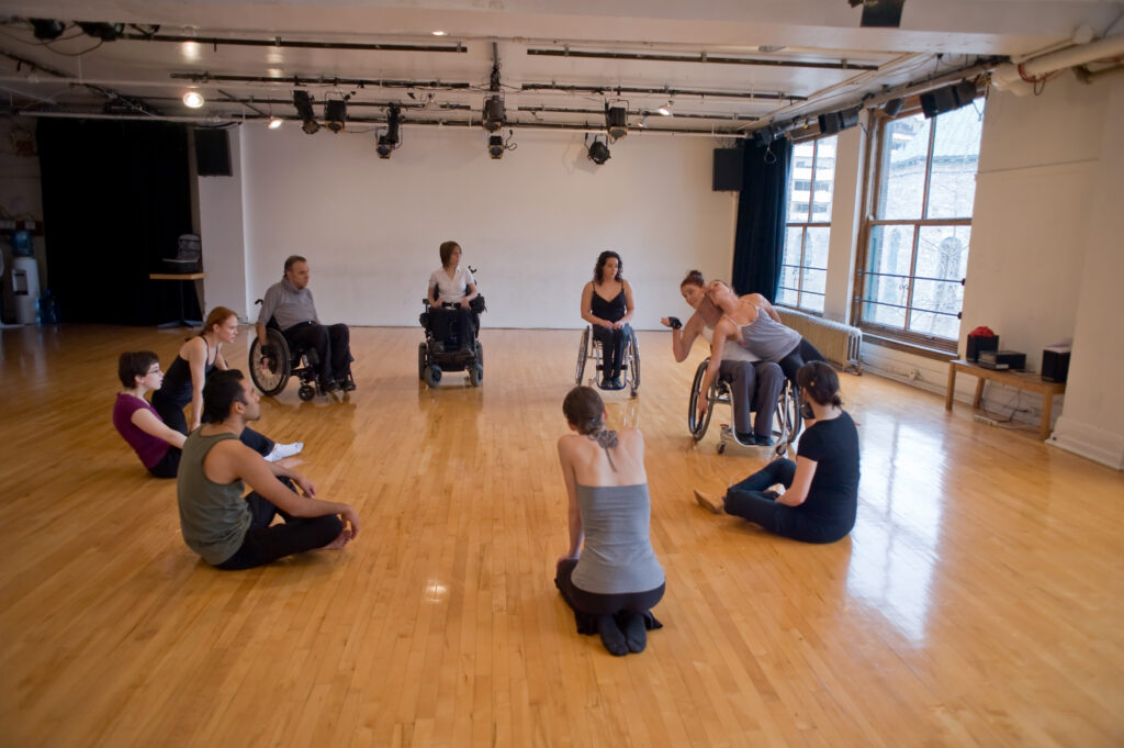 Ateliers : un groupe de personnes assises en cercle. France Geoffroy, enseignante, fait une démonstration de mouvement de portée avec Joannie Douville, co-enseignante.