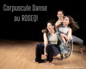 Quand tu me regardes, trio qui rit. Trois artistes se produisent sur une scène en bois sur fond sombre. Une femme en fauteuil roulant sourit largement, un homme se penche sur son épaule et une autre femme est accroupie à côté d'eux, tous riant et affichant des expressions de joie et d'énergie. Leur tenue est décontractée et confortable.