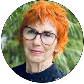 En couleur, de face, cadrée jusqu'au cou, Marthe Boulianne a la peau pâle, les cheveux courts orange vif. Elle porte de large lunette brunes et un léger rouge-à-lèvres rosé. Elle est postée devant un arbre vert.